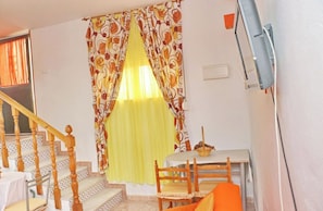 Une pièce avec un escalier, une table à manger entourée de chaises et une fenêtre ornée de rideaux à motifs.
