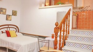 A bedroom with a bed, a chair, a wooden staircase, and a small table with a plant. - El Rinconcito de Pepa I,close to the beach (Conil de la Fra.)