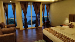 A bedroom with a large bed, a sofa, and a chair. There are curtains on the windows, and a balcony is visible. - Divsai Retreat (Gyalshing)