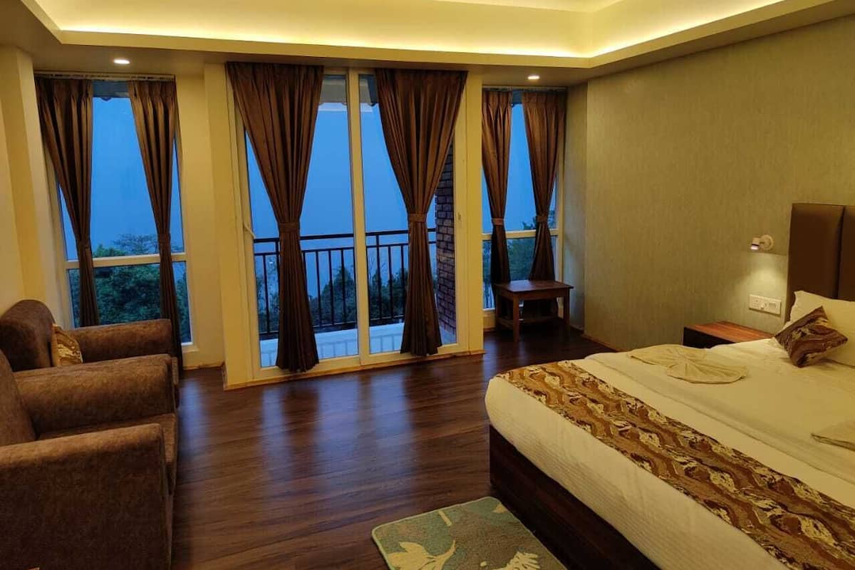 A bedroom with a large bed, a sofa, and a chair. There are curtains on the windows, and a balcony is visible.