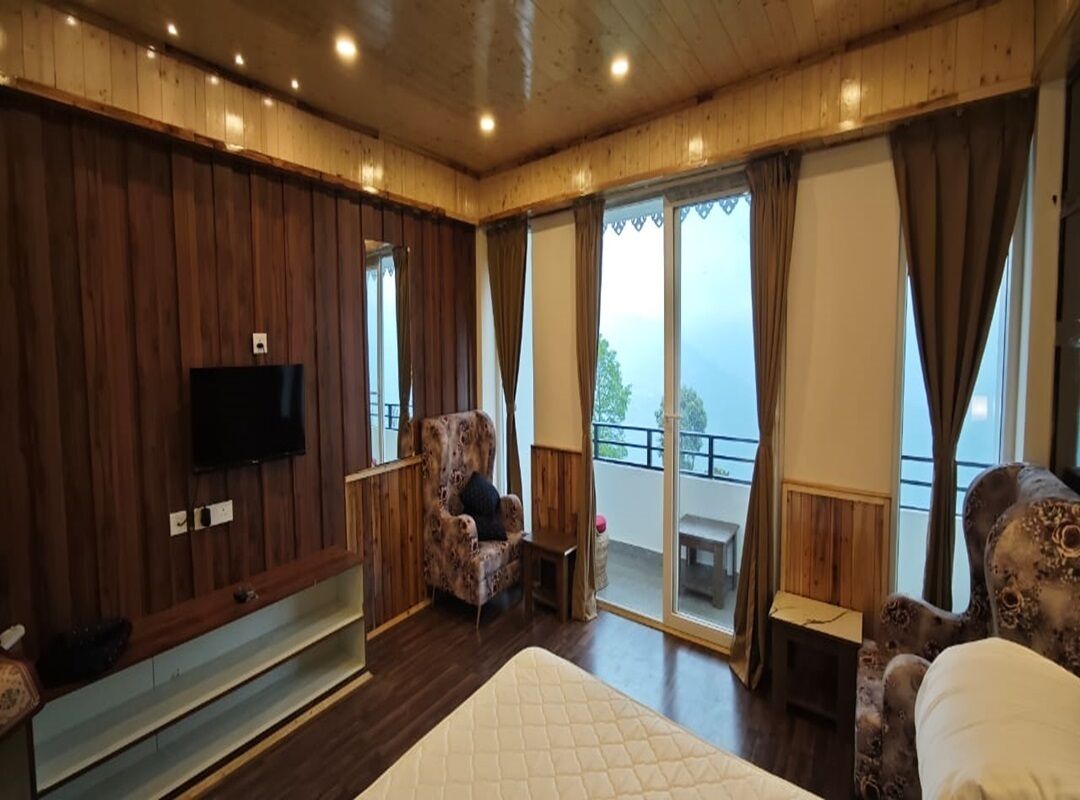 A wooden-paneled room with a bed, a television, a chair, and a balcony with curtains.