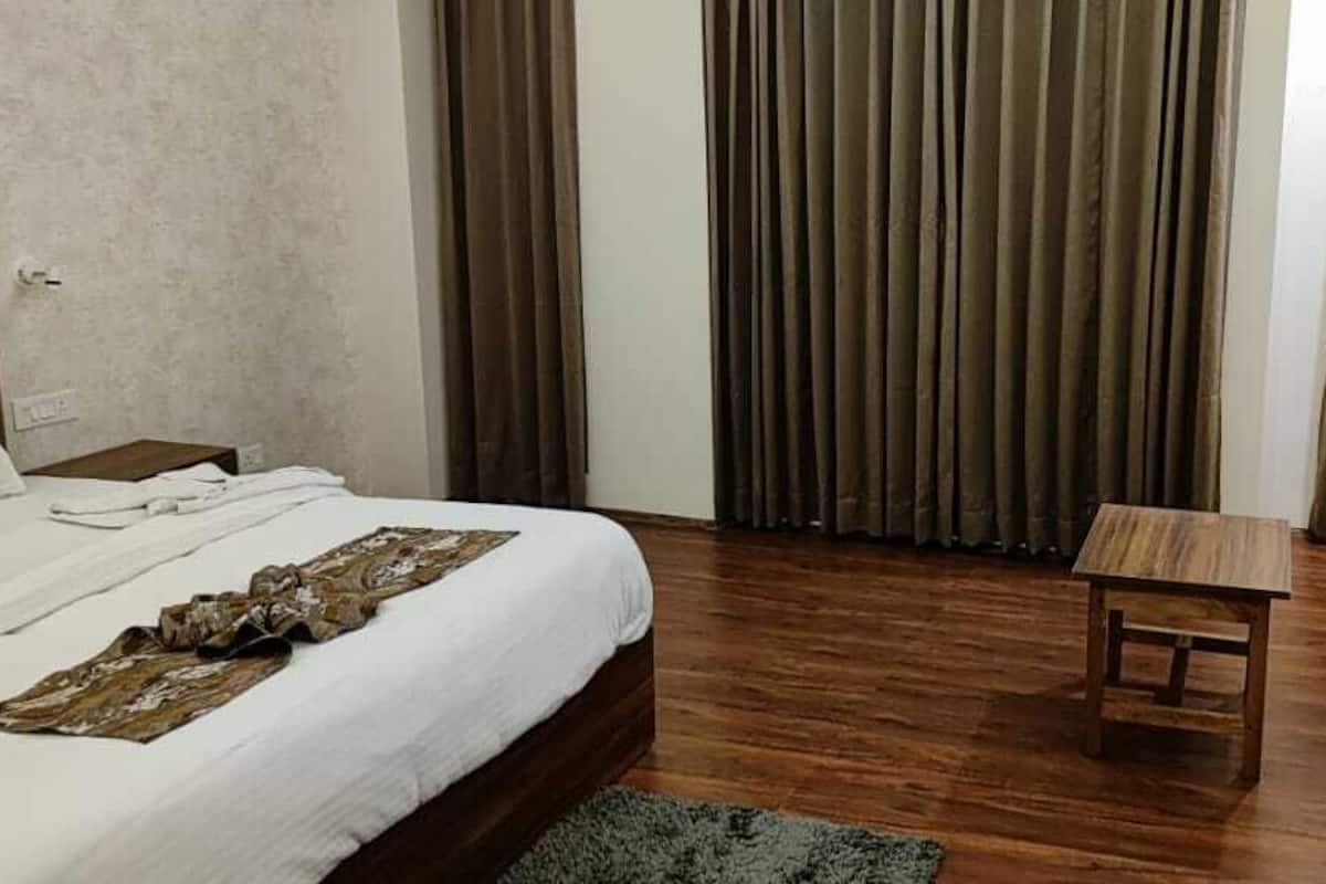 A hotel room with a bed, a small wooden table, two armchairs, and a window with curtains.
