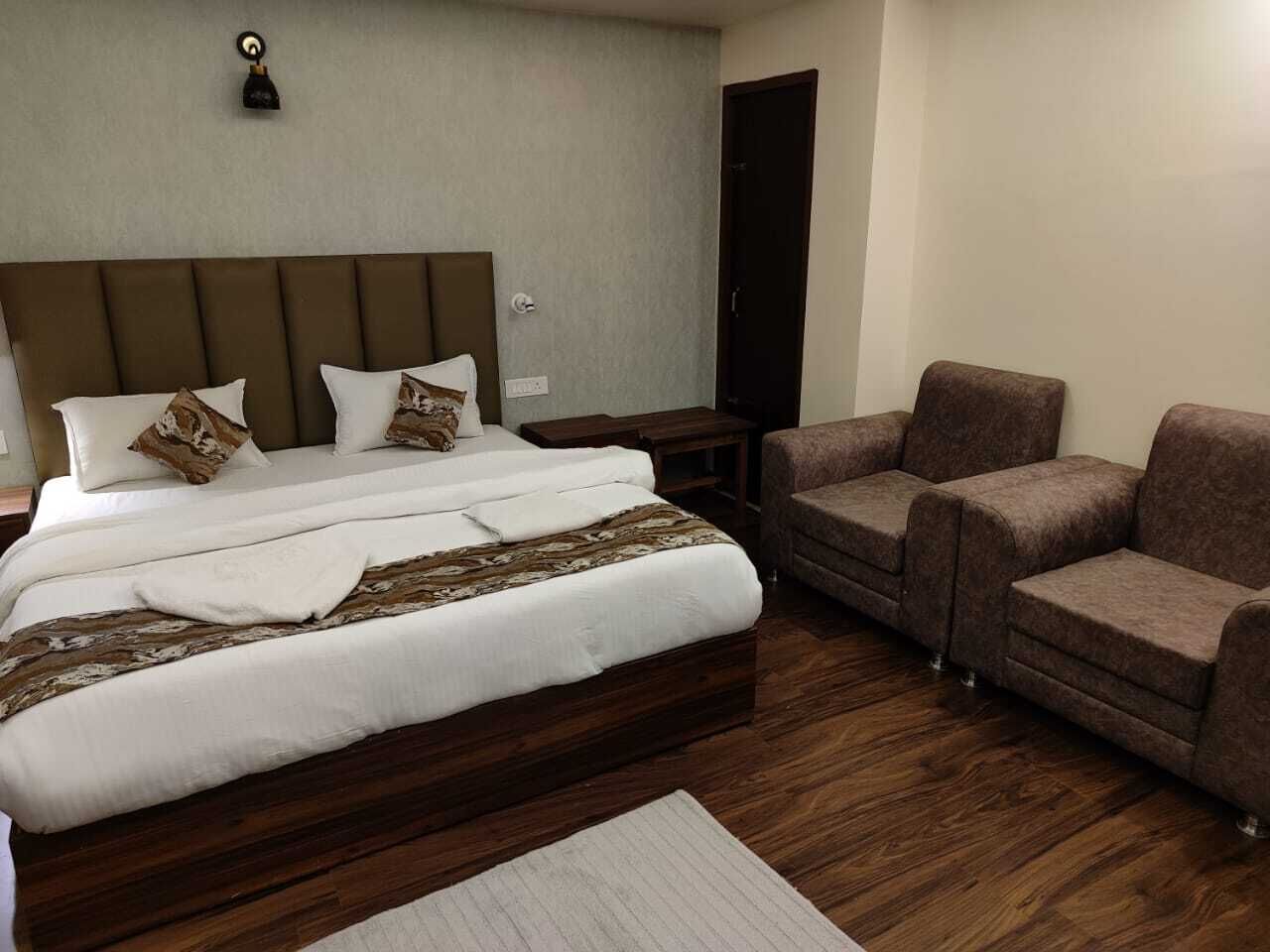 Una habitación de hotel con una cama grande, dos sillones, una mesita y suelo de madera.