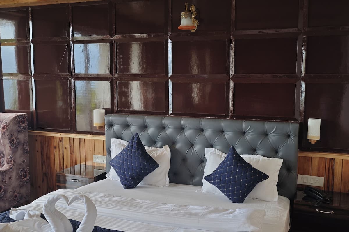 A bedroom with a tufted headboard, a wooden nightstand, a floral armchair, and a large window.