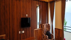 A wooden-paneled room with a television mounted on the wall, a patterned armchair, and a small table. - Divsai Retreat (Gyalshing)
