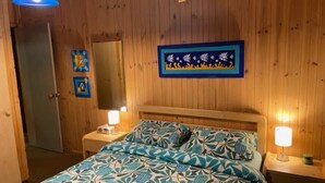 A bedroom with wooden walls, a bed with a floral bedspread, two bedside lamps, and a framed picture above the bed. - Sandy Point Log Cabin (Sandy Point)