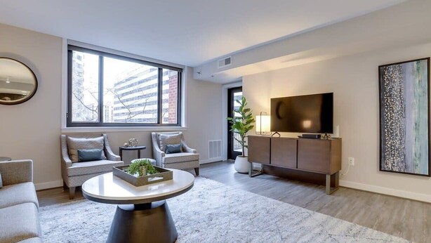 A modern living room with a large window, a round coffee table, sofas, a TV, and a cabinet. - Sojourn  Courtland Towers w/ Private Balcony (Arlington)