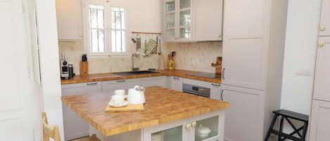 A kitchen with white cabinets, a wooden island, and a black stool.