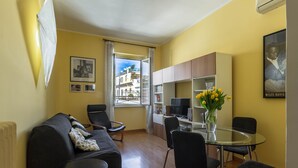 Ein kompakter Wohnraum mit einer Couch, einem Esstisch mit Stühlen, einem Fernseher und einem Bücherregal.
