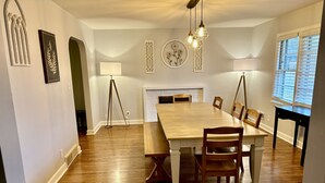 Un comedor con una mesa y sillas de madera, una lámpara de pie y decoración en la pared.