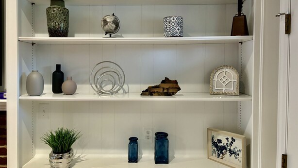 Un estante blanco con objetos decorativos, incluyendo jarrones, un globo terráqueo y un cuadro enmarcado.