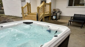Un jacuzzi en un patio trasero con terraza de madera y una parrilla.