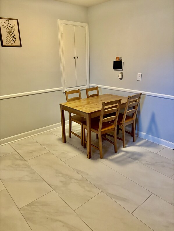 Un comedor con mesa y sillas de madera, una puerta blanca y un interruptor de luz en la pared.