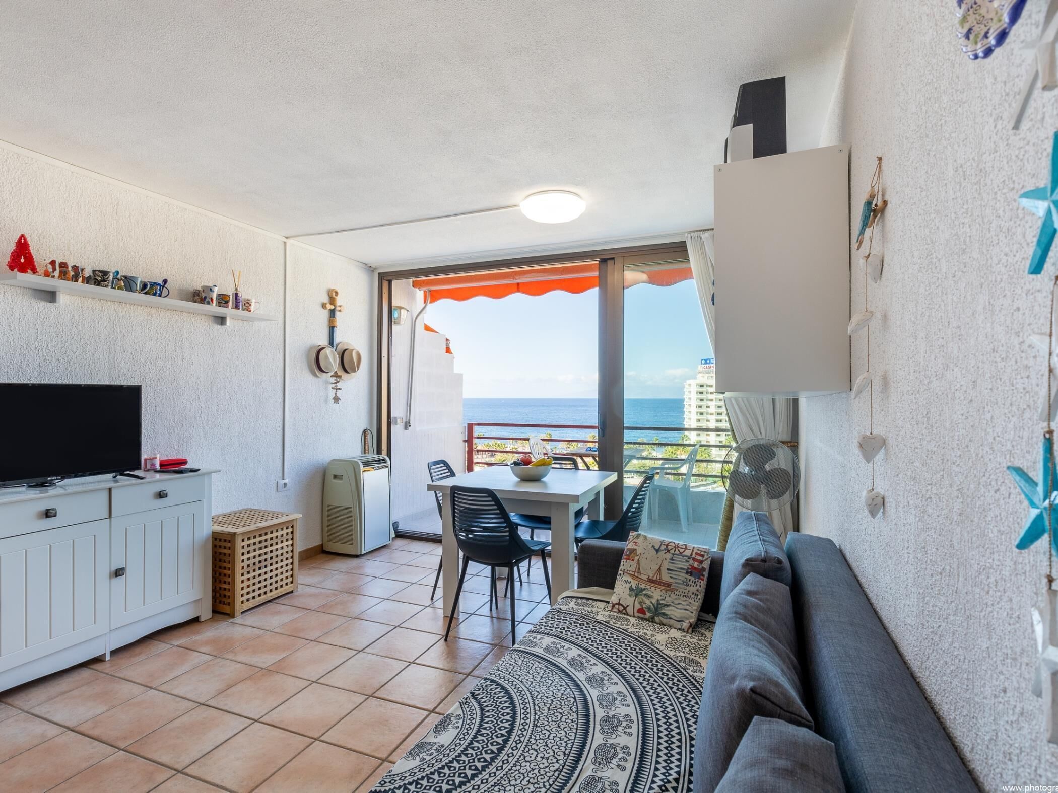 Een knus woongedeelte met een televisie, kitchenette, eethoek en een balkon met uitzicht op zee.