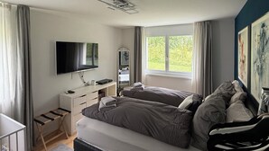 Makuuhuoneessa on sänky, työpöytä, televisio ja ikkuna, jossa on verhot.