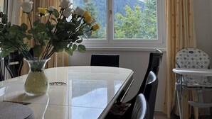Ruokailutila, jossa on pöytä, tuoleja, maljakko kukkineen ja näkymä vuorille ikkunasta.