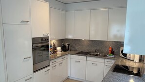 Moderni keittiö, jossa on valkoiset kaapit, graniittitaso, sisäänrakennettu uuni ja puinen leikkuulauta.