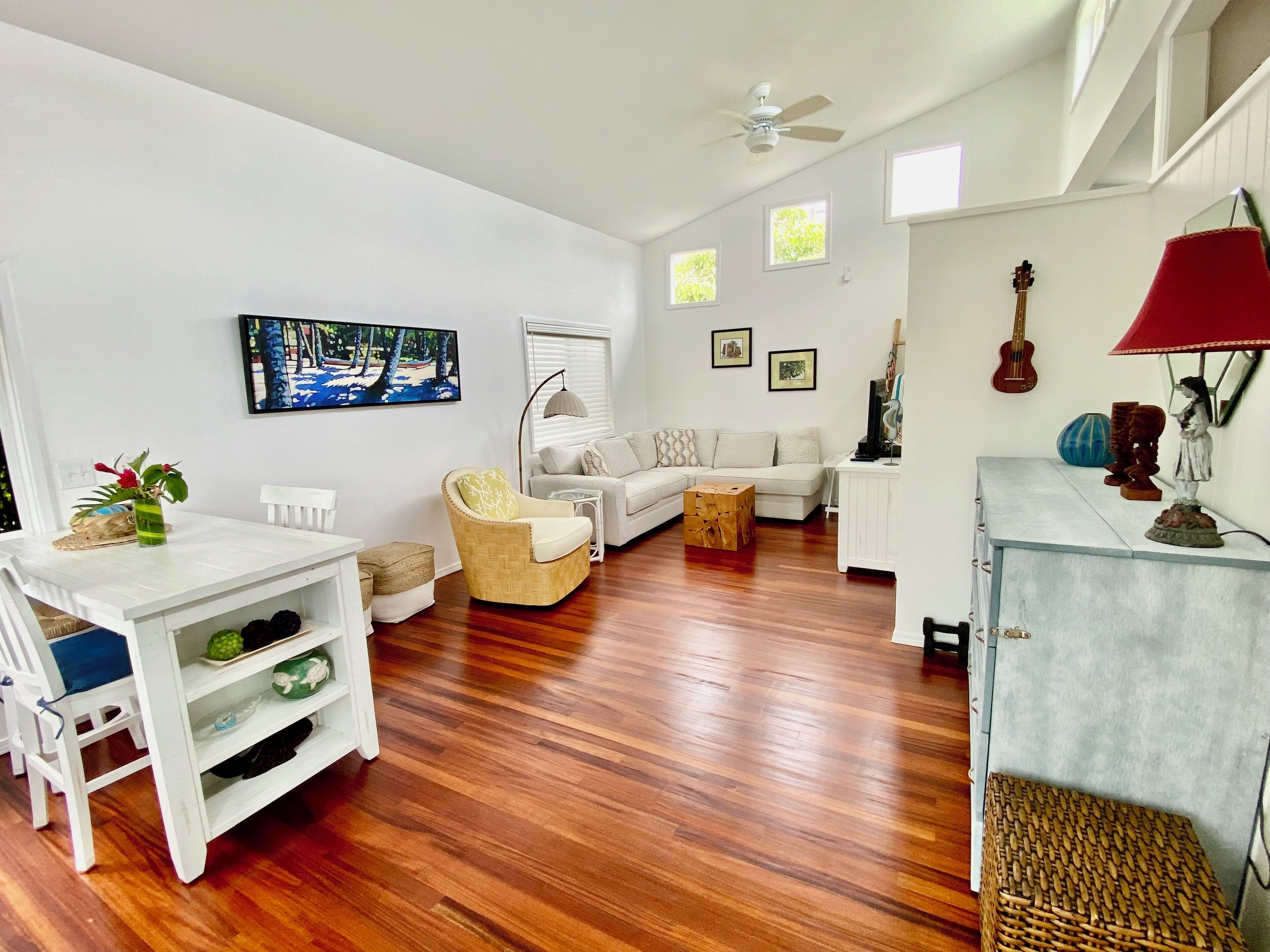Un salon spacieux avec un canapé blanc, un fauteuil en osier, une table à manger avec des chaises et un ventilateur de plafond.