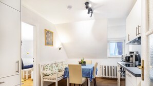 Eine kleine Küche mit Essbereich, weißen Schränken und Blick durch ein Fenster.