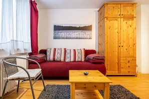 Ein Zimmer mit einem roten Sofa, einem Holzschrank, einem Sessel und einem Tisch.