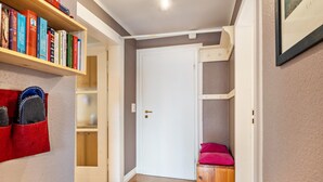 Ein Flur mit Bücherregal, einer Tür und einer kleinen Holzbank mit rosa Kissen.