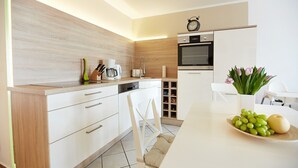 Eine moderne Küche mit Holzausschlag, weißen Schränken, einem eingebauten Ofen und einem Essbereich mit einem weißen Stuhl und Tisch.