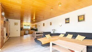 Un'ampia zona giorno con soffitto in legno, un divano, un tavolino da caffè e una cucina sullo sfondo.
