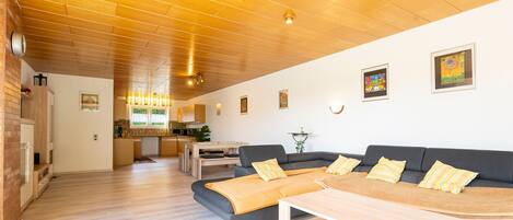 Un vaste espace de vie doté d’un plafond en bois, d’un canapé, d’une table basse et d’une cuisine à l’arrière-plan.