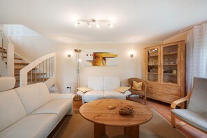 A modern living room with a white sofa, a wooden coffee table, a cabinet with glass doors, and a staircase. - Holiday Home "Zwischen Den Seen" with Private Terraces, Garden and Wi-Fi (Wiefelstede-Dringenburg)
