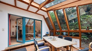 A dining area with a wooden table and chairs, large windows, and a view of greenery outside. - Holiday Home 'Ferienhaus Am Brandorffsee' with Lake View, Private Terrace & Garden (Wiefelstede)