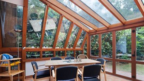 A conservatory with a wooden table and chairs, large windows, and a view of greenery. - Holiday Home 'Ferienhaus Am Brandorffsee' with Lake View, Private Terrace & Garden (Wiefelstede)