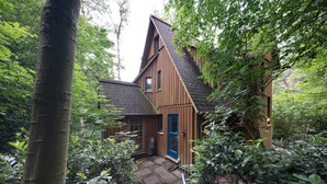A wooden house with a blue door, surrounded by dense foliage. - Holiday Home 'Ferienhaus Am Brandorffsee' with Lake View, Private Terrace & Garden (Wiefelstede)