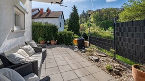 Eine Terrasse mit Gartenmöbeln, gefliestem Boden, einem Zaun und einem Haus im Hintergrund.