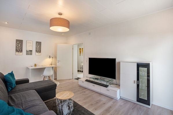 Un salon moderne comprenant un canapé, un téléviseur, un meuble et une petite table.