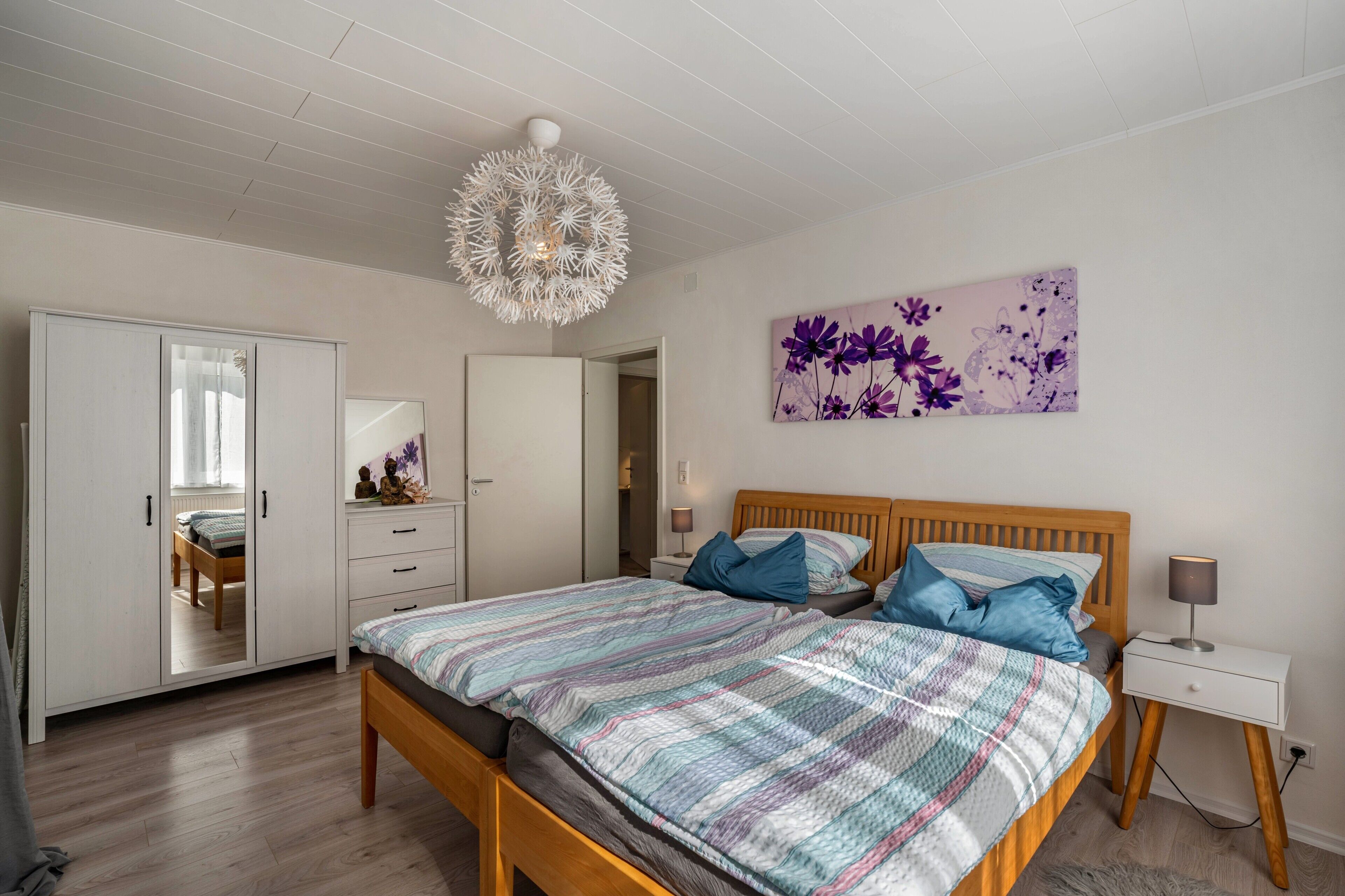 Un dormitorio con cama, mesita de noche, lámpara y una pared decorada con un cuadro floral.