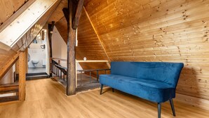 Un interno in legno con un divano blu, travi a vista e una scala che conduce a un livello superiore.