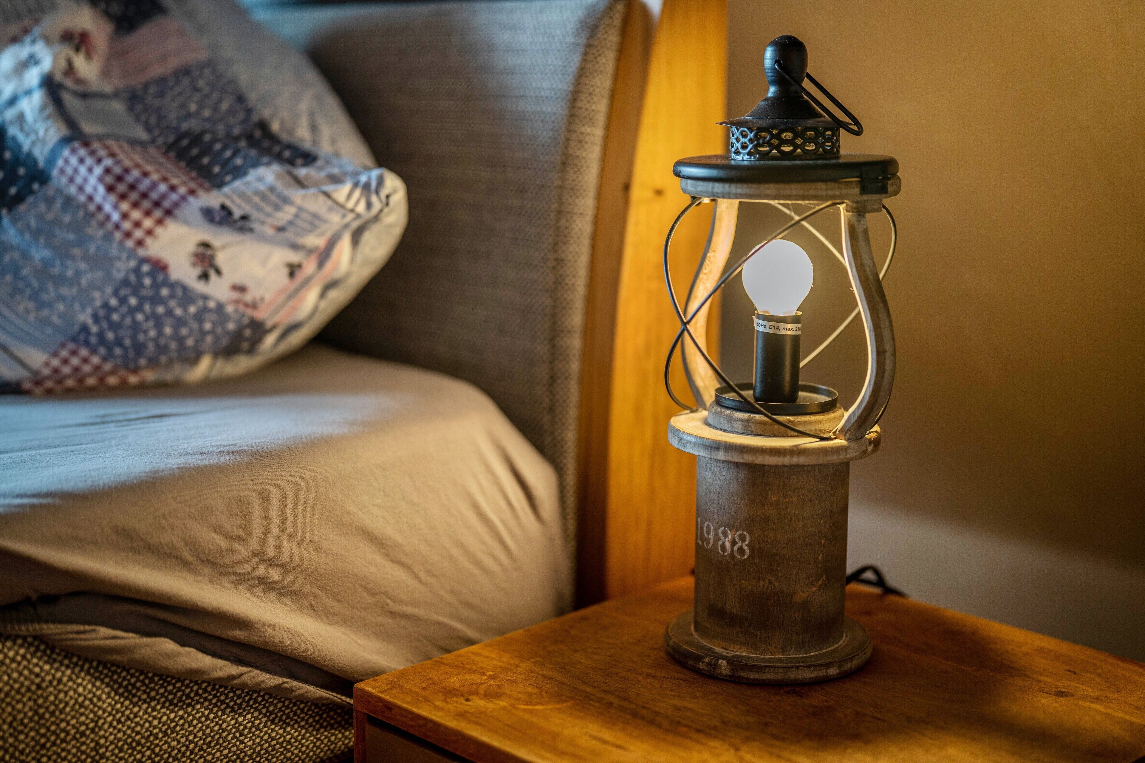 Een lamp in vintage-stijl op een houten nachtkastje naast een bed met een gestreept kussen.