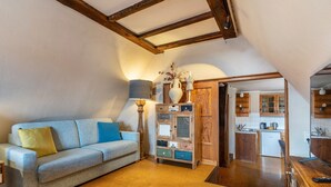 Een woonkamer met een bank, een lamp, een houten kast en een keuken op de achtergrond.