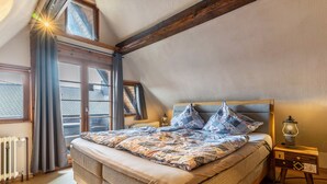 Een slaapkamer met een groot bed, een nachtkastje met een lamp, een raam met gordijnen en een radiator.