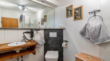 Un baño con tocador de madera, un lavabo blanco, un inodoro y un espejo. Hay toallas colgadas en un perchero y un cuadro en la pared.