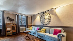 A living room with a sofa, a wooden cabinet, a clock, and a radiator. - Weissburgunder Superior Apartment 52 sqm, City View, up to 4 Guests, Optional Breakfast, 3D Tour (Vogtsburg)