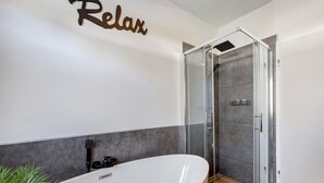 Ein modernes Badezimmer mit einer freistehenden Badewanne, einer in Glas abgeschirmten Dusche und einem Schild mit der Aufschrift 'Relax'.