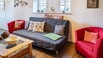 Ein gemütliches Wohnzimmer mit grauem Sofa, roten Sesseln, einem Holztisch und einem Fenster mit Dekoration.