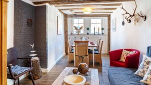 A cozy living room with a sofa, a dining table with chairs, a wooden coffee table with a bowl, and a red armchair. - Vacation Home "Gästehaus Vis À Vis" with Mountain View, Shared Garden & Wi-Fi (Wallhausen)