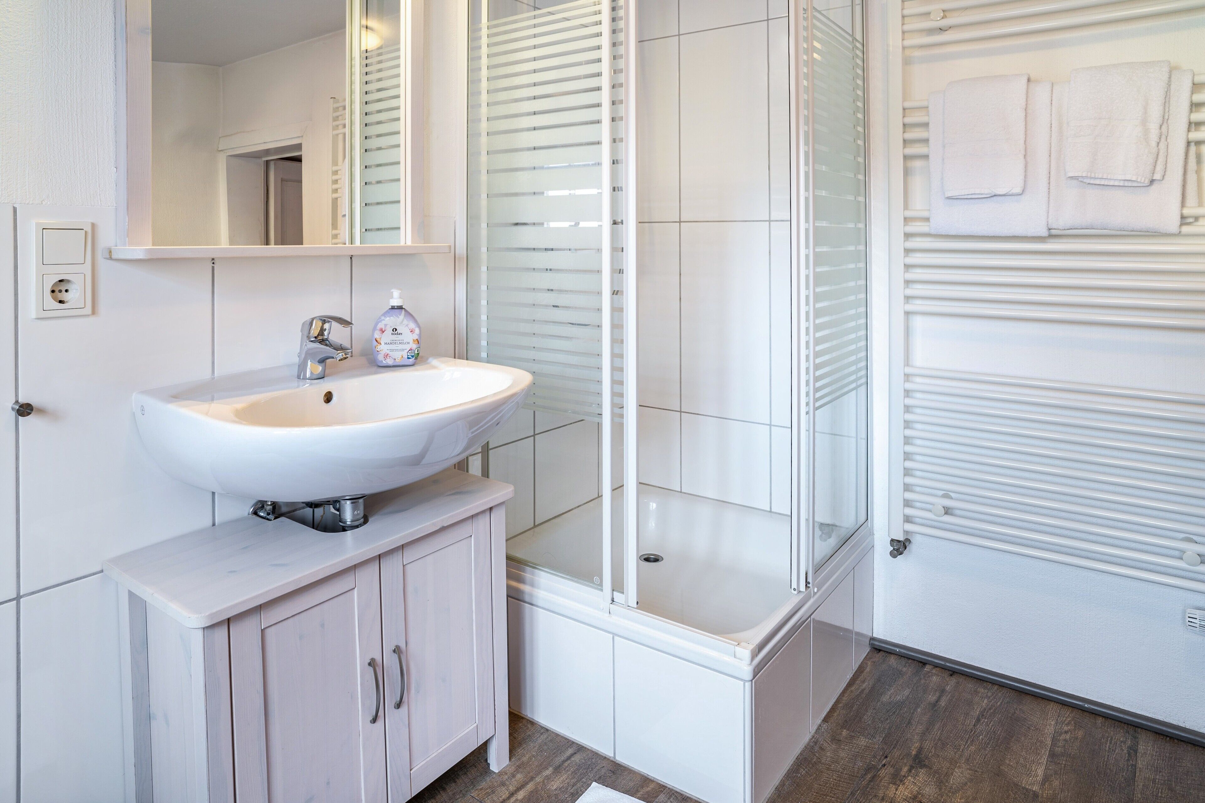 A modern bathroom with a white sink, mirror, and glass shower enclosure.