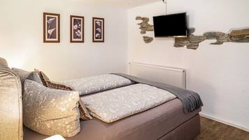 A bedroom with a bed, a television mounted on a stone wall, and three framed pictures on the wall.