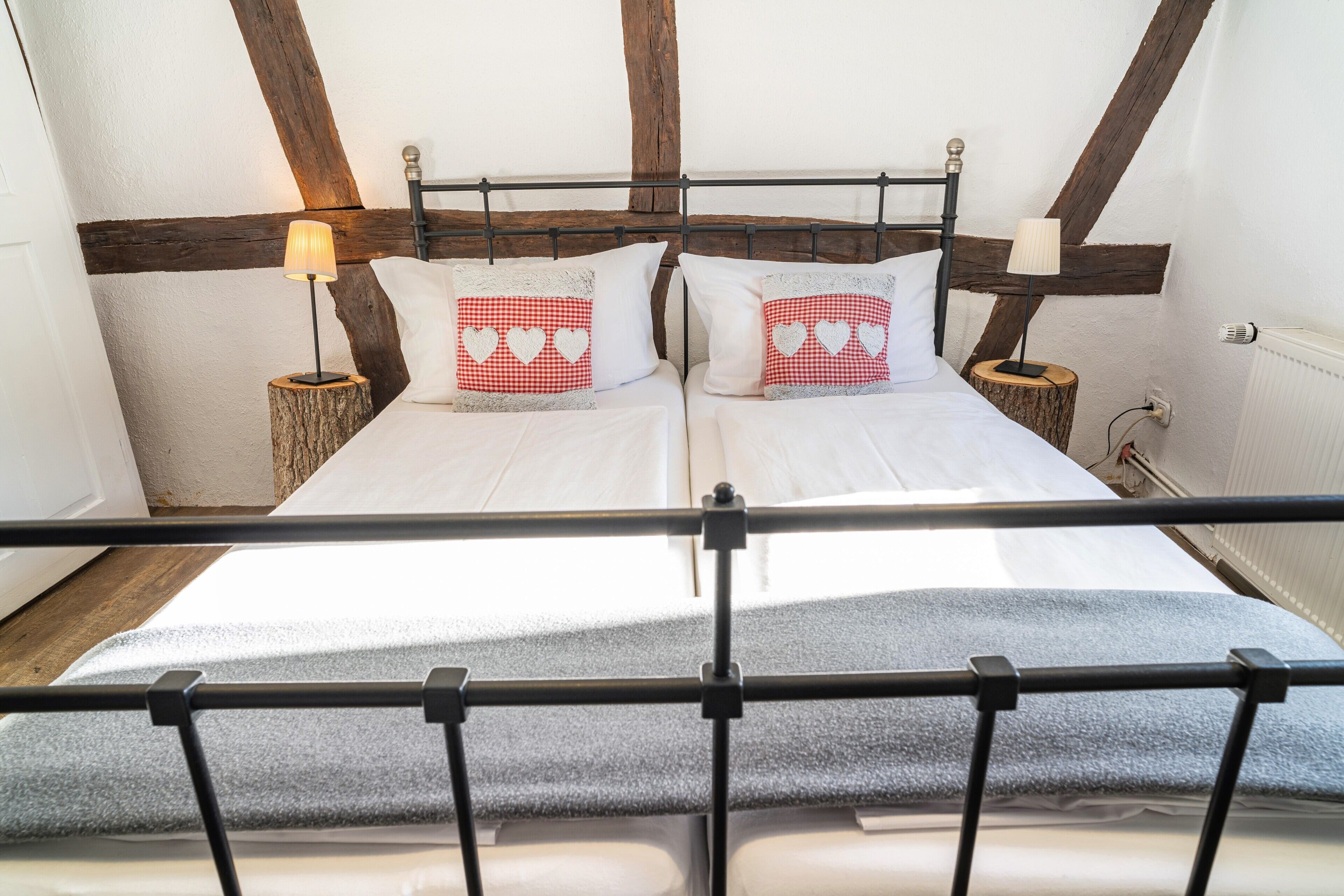 Ein Doppelbett mit Holz-Kopfstück, zwei Nachttische mit Lampen und Blick auf die geneigten Decken des Zimmers.