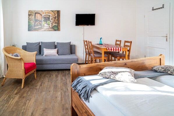 Une pièce comprenant un lit, un canapé, une table à manger avec des chaises, un téléviseur et un tableau accroché au mur.