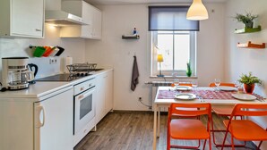 A compact kitchen with white cabinets, a stove, and a dining area with orange chairs and a table. - Holiday Apartment "4" with Mountain View, Shared Garden & Wi-Fi (Wallhausen)