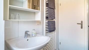 A bathroom with a white sink, a glass shelf, a towel rack, and a door.